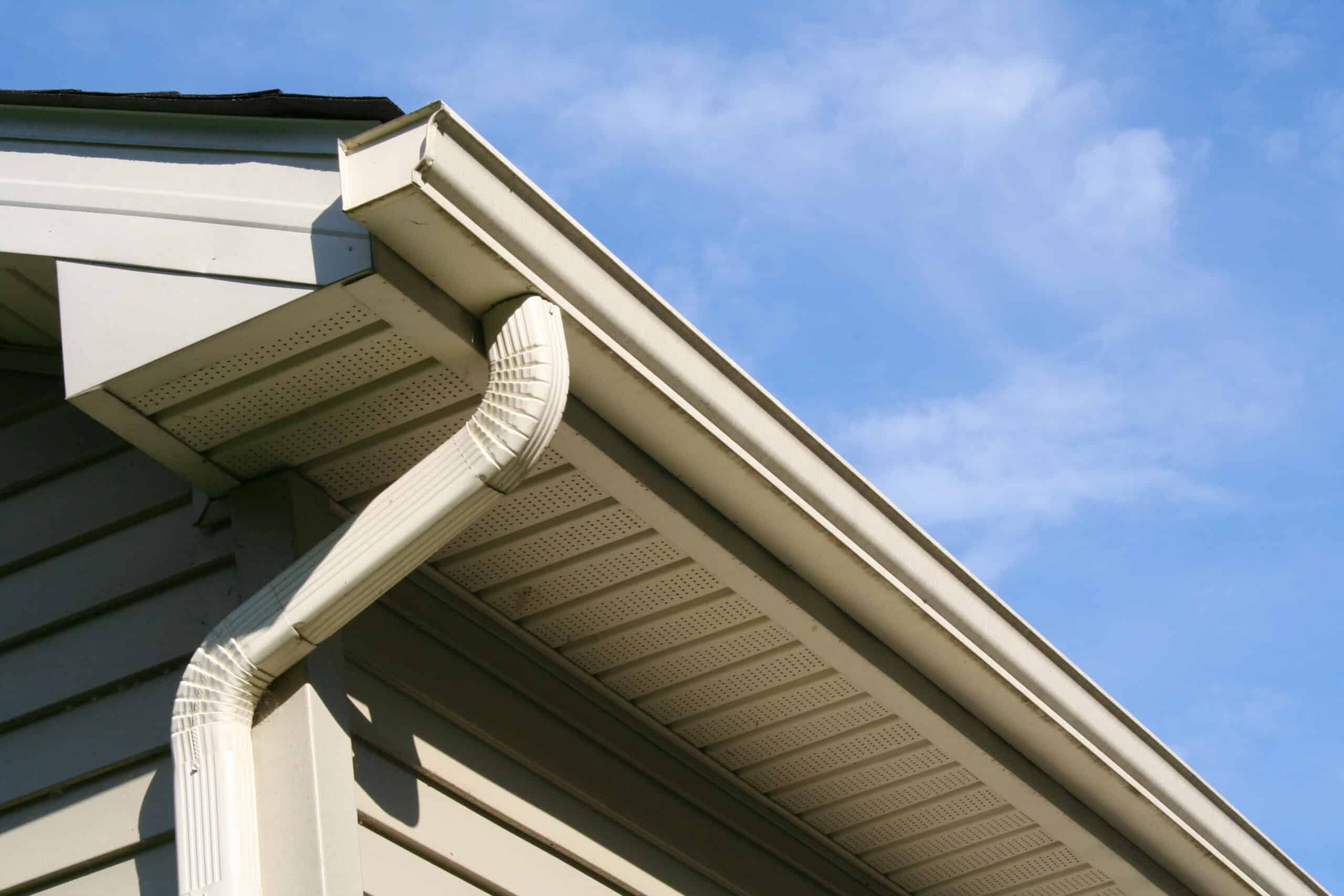 Angled view of gutter and downspout on a house. Blue sky in background.